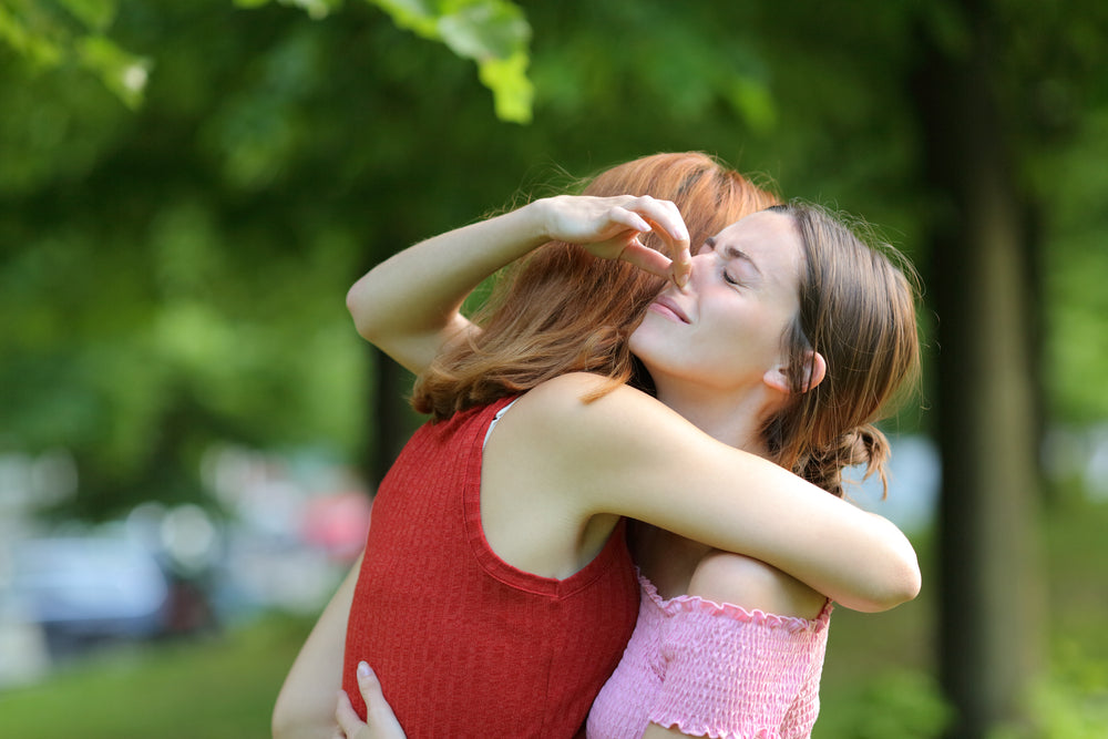 Two women hugging and one is holding her nose as her friend smells